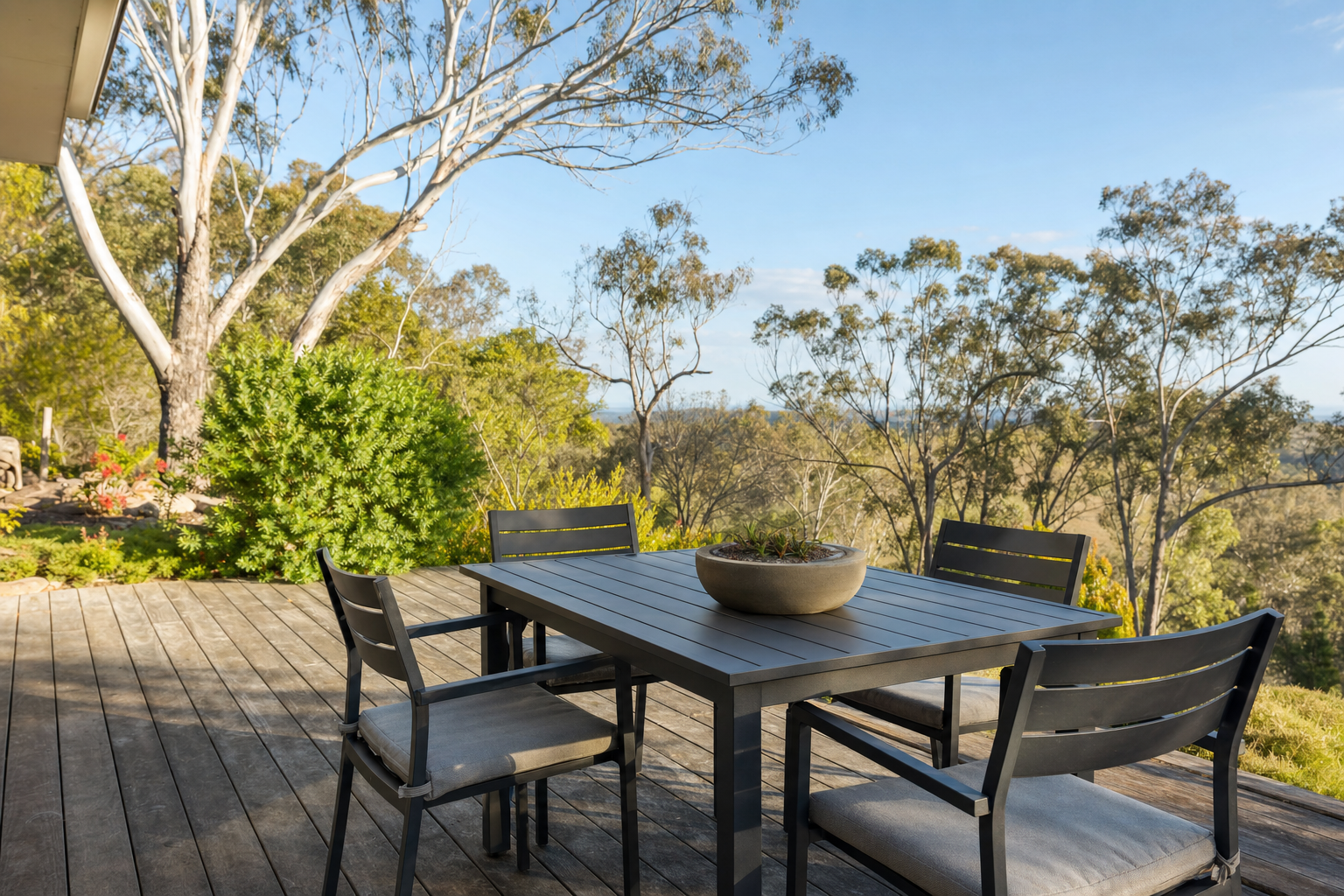 Charcoal powder coated aluminium outdoor dining setting with cushions on a weathered timber deck, gum trees and Australian bushland behind